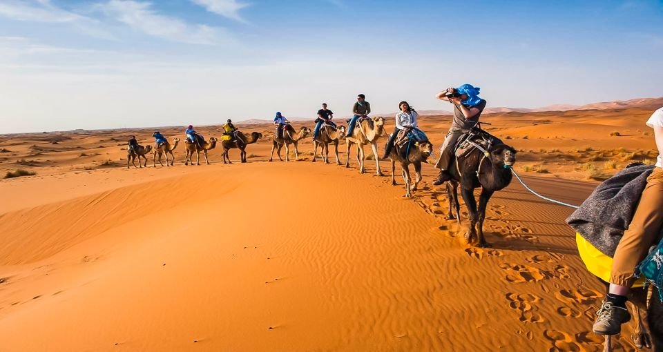 Photo of a camel ride: This photo shows a group of tourists enjoying a trip on camel backs in the desert, where they are exploring the enchanting landscape and enjoying a unique and enjoyable experience.